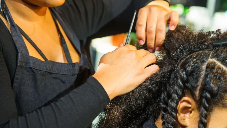 Close up african hairstylist braided hair of afro american female client in the barber salon. Black healthy hair culture and Style. Stylish therapy professional care concept. Selective focus