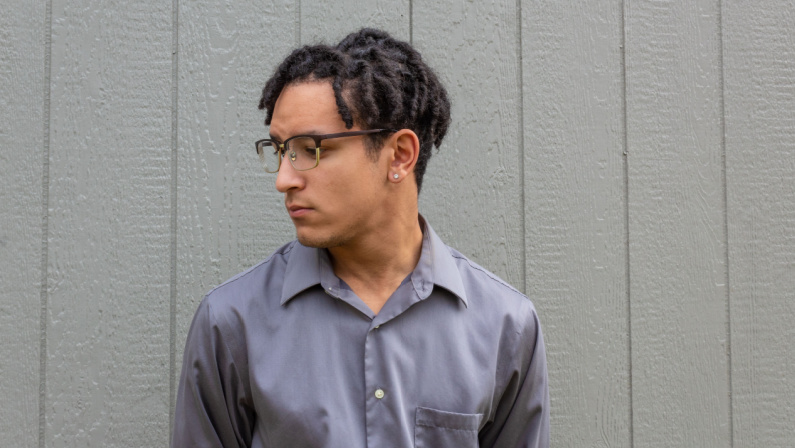 Multiracial young man in eyeglasses, profile view with natural hair in dreadlock twists, serious demeanor, horizntal aspect