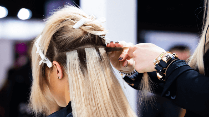 Professional hairdresser making hair extensions for blonde girl in a beauty salon