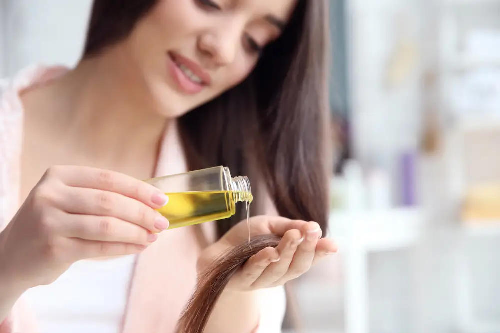 Young woman applying oil onto hair at home 